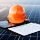 Orange safety helmet on solar panels with clipboard.