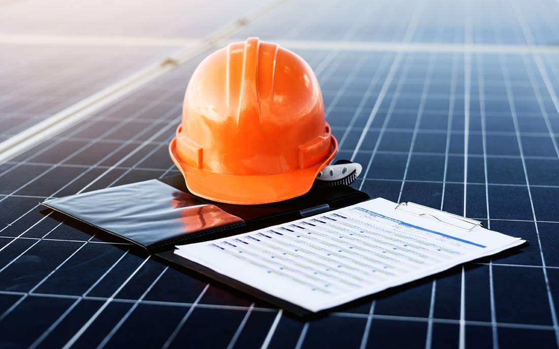 Orange safety helmet on solar panels with clipboard.
