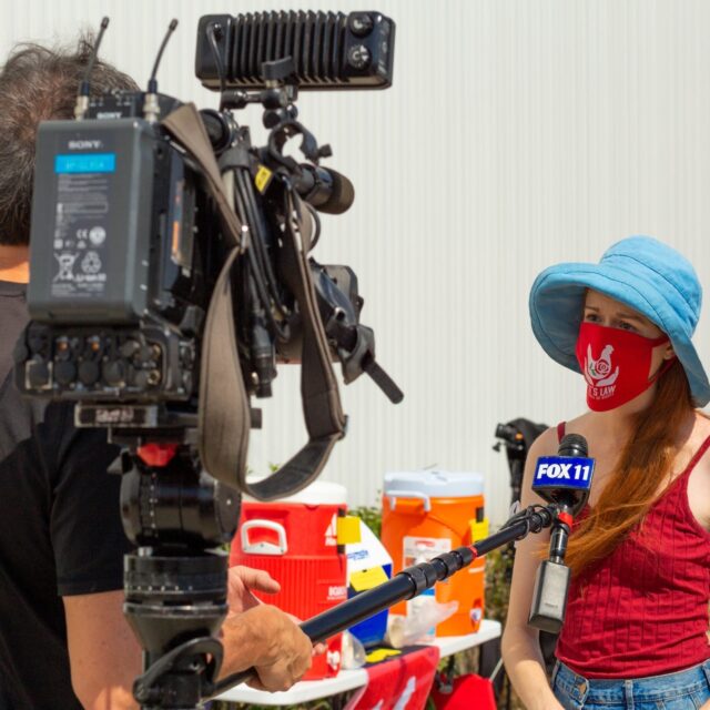 A young woman in a blue hat and red mask being interviewed by a news crew.