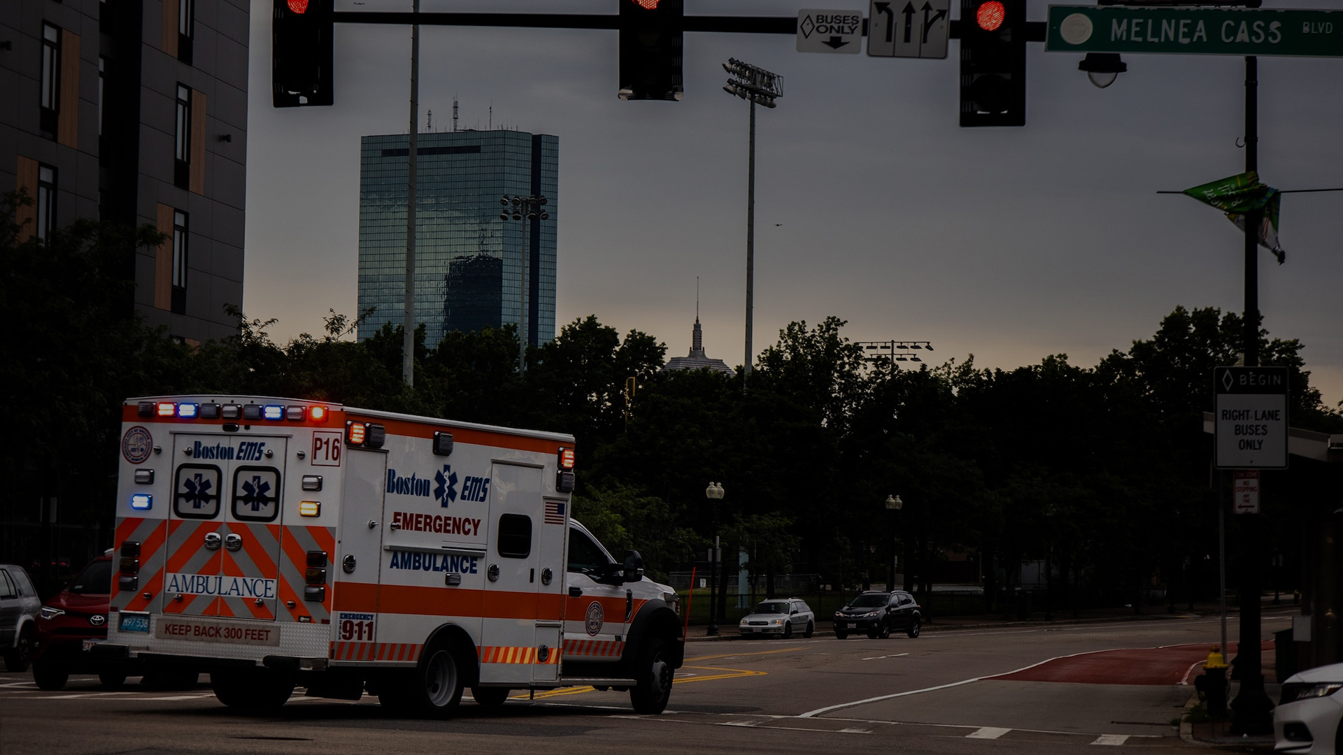 Ambulance with lights on at evening intersection near tall building.
