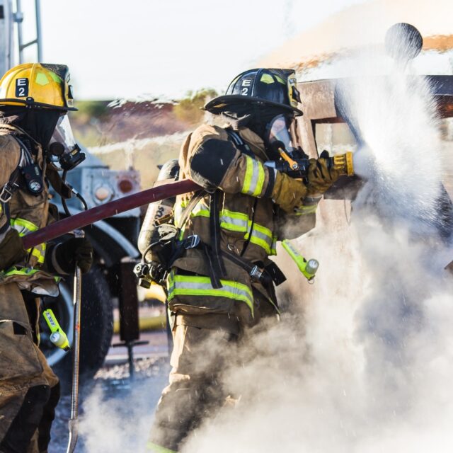 Firefighters in full gear extinguishing a fire with a hose.