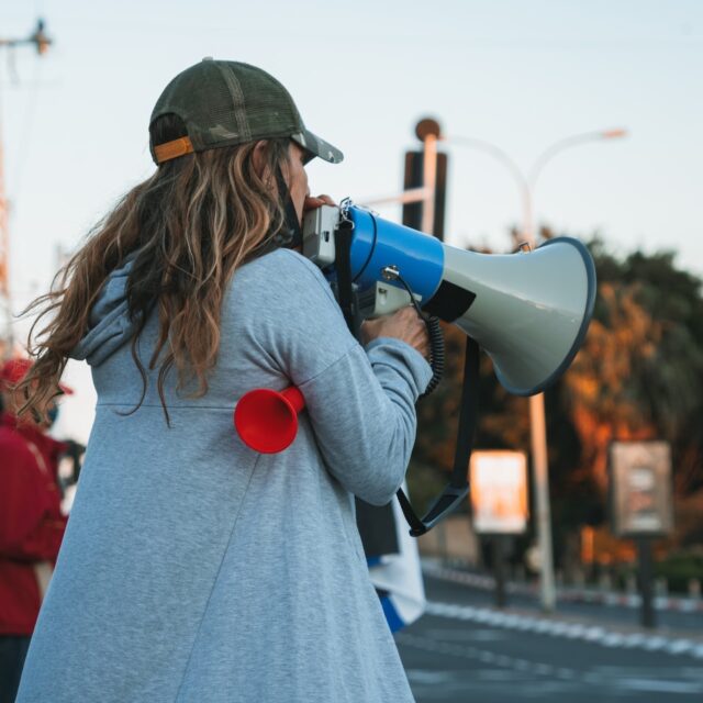 Woman speaking through a megaphone outdoors.